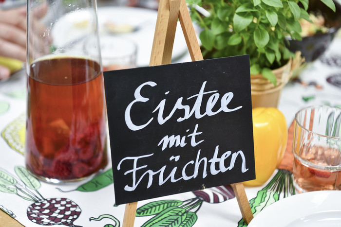Foto: Sarah Wiener Stiftung | Thomas Panzau Ein Schild mit der Aufschrift "Eistee mit Früchten" vor einer Karraffe