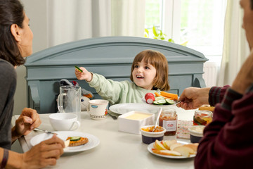 Foto: Sarah Wiener Stiftung | photothek Familie frühstückt gemeinsam am Esstisch. Kind probiert Gemüse.